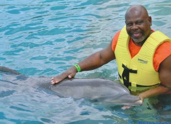 Man in life jacket petting dolphin