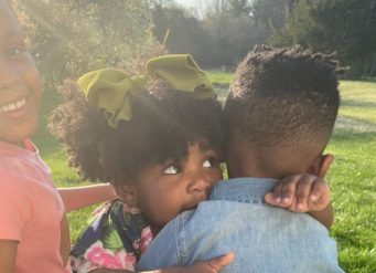 Three children playing outdoors in sunlight.